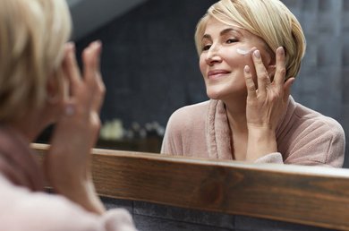 Vrouw voor de spiegel smeert creme op